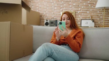 Young redhead woman smiling confident using smartphone at new home