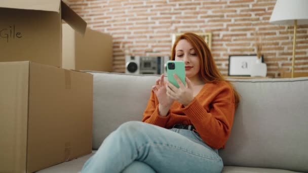 新しい家でスマートフォンを使って自信を持って笑顔若い赤毛の女性 — ストック動画