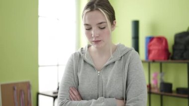 Young blonde woman standing with relaxed expression at sport center