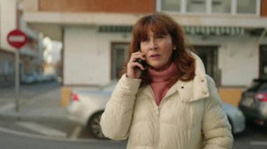 Middle age redhead woman talking on the smartphone at street