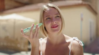 Young blonde woman smiling confident listening audio message by the smartphone at street