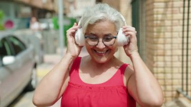 Orta yaşlı, kır saçlı, müzik dinleyip sokakta dans eden bir kadın.