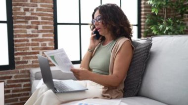 Middle age hispanic woman doing countability with documents and laptop