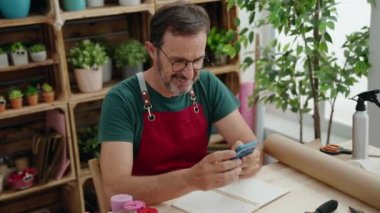 Çiçekçiye akıllı telefon kullanarak gülümseyen orta yaşlı bir çiçekçi.