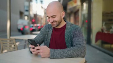 Young bald man smiling confident using smartphone at coffee shop terrace