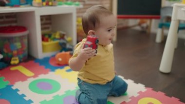 Adorable hispanic baby playing with car toy sitting on floor at kindergarten