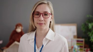 Young blonde woman preschool teacher smiling confident standing with arms crossed gesture at kindergarten