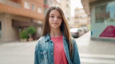 Sevimli kız gülümsüyor. Kendine güveniyor, kalp hareketi yapıyor. Sokakta elleriyle.