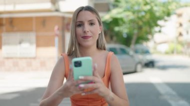Genç ve güzel İspanyol kadın gülümsüyor. Kendine güveni tam. Sokakta akıllı telefonun yanında selfie çekiyor.
