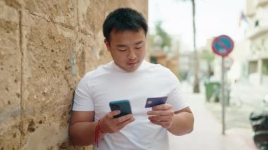 Young chinese man using smartphone and credit card at street