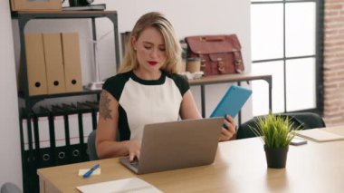 Young beautiful hispanic woman business worker using laptop and touchpad at office