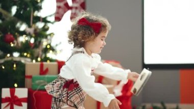 Adorable hispanic girl playing tambourine standing by christmas tree at home