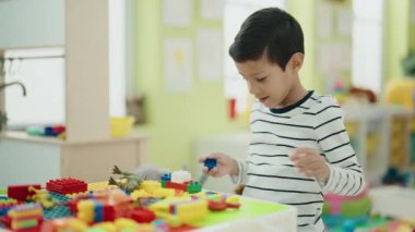 Adorable hispanic boy playing with construction blocks standing at kindergarten