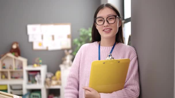 Young Chinese Woman Preschool Teacher Smiling Confident Holding Clipboard Kindergarten — Vídeo de Stock
