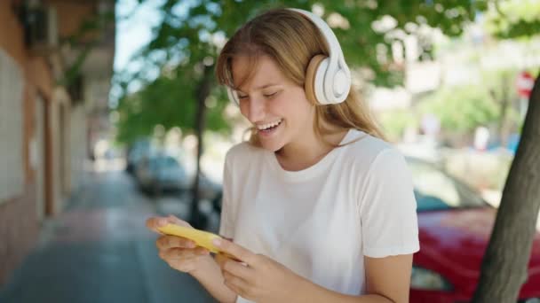 年轻的金发女孩笑着自信地在街上看智能手机视频 — 图库视频影像