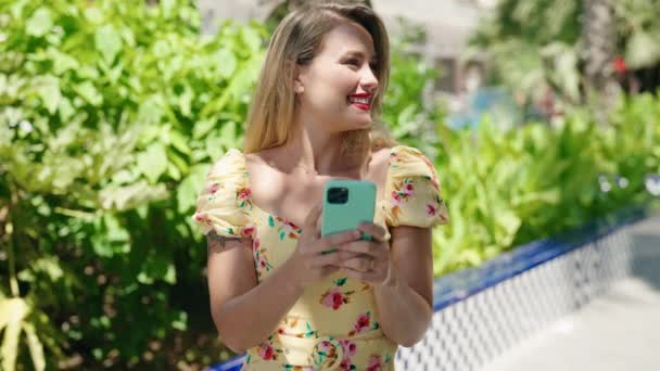 年轻美丽的惊慌失措的女人在公园用智能手机充满自信地微笑 — 图库视频影像