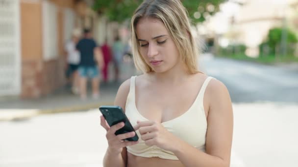 年轻的金发女人在街上用智能手机充满自信地微笑 — 图库视频影像