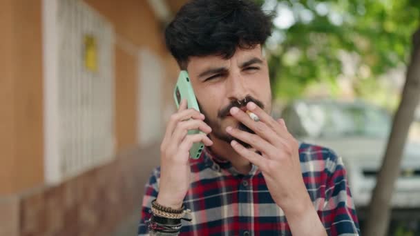 Young Hispanic Man Talking Smartphone Smoking Street — Stockvideo