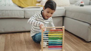 Adorable hispanic boy playing with abacus sitting on floor at home
