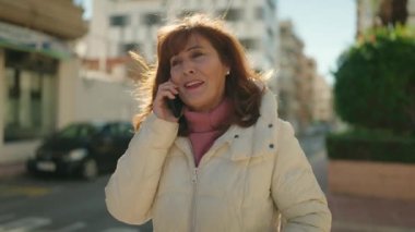 Middle age redhead woman smiling confident talking on the smartphone at street