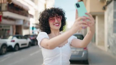 Orta Doğulu genç bir kadın sokakta akıllı telefon kullanarak gülümsüyor.