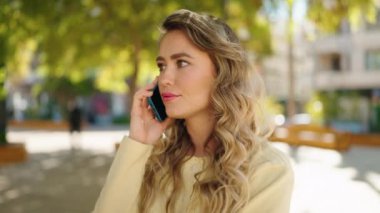Young blonde woman worried talking on the smartphone at park