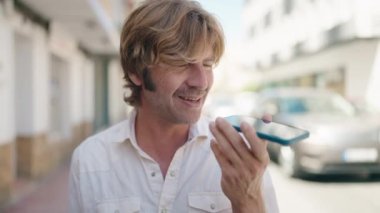 Genç adam gülümsüyor. Kendine güveniyor. Sokakta akıllı telefondan konuşuyor.