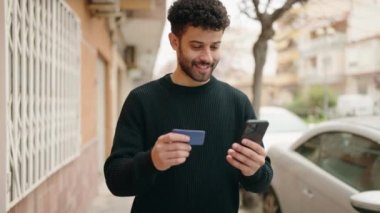 Sokakta akıllı telefon ve kredi kartı kullanan genç bir Arap.