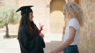 Two women mother and graduated daughter high five with hands raised up at campus university