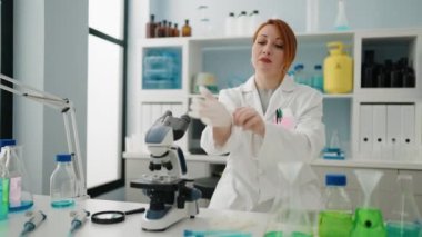 Laboratuvarda bilim adamı üniforması ve eldiven giyen kızıl saçlı genç bir kadın.