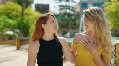 Two women hugging each other speaking and walking at park