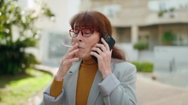 Middle age woman business executive talking on the smartphone smoking cigarette at street