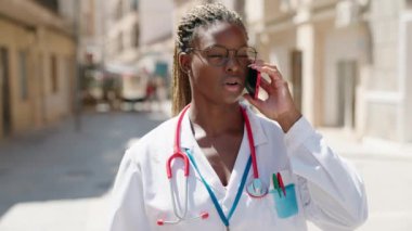 Afro-Amerikalı kadın doktor sokakta akıllı telefondan konuşuyor.