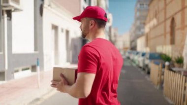 Young hispanic man deliveryman holding package at street