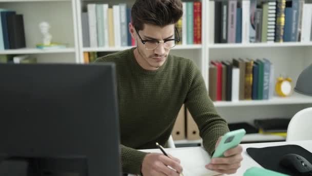 Jovem Estudante Hispânico Usando Escrita Smartphone Notebook Universidade Biblioteca — Vídeo de Stock