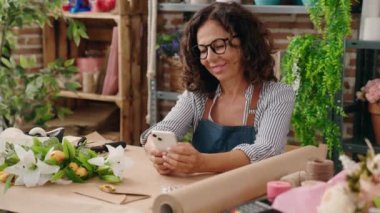 Middle age woman florist smiling confident using smartphone at flower shop