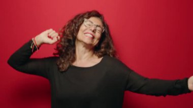 Middle age woman smiling confident dancing over red background