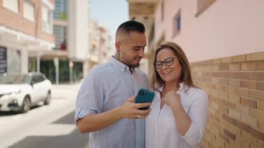 Kadın, erkek, anne ve kız sokakta akıllı telefondan selfie çekiyorlar.