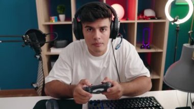 Young hispanic man streamer playing video game using joystick at gaming room