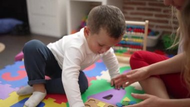 Adorable toddler playing with puzzle game sitting on floor at kindergarten