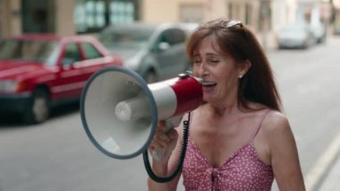 Middle age woman using megaphone screaming at street