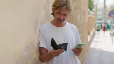 Young blond man using smartphone holding passport at street