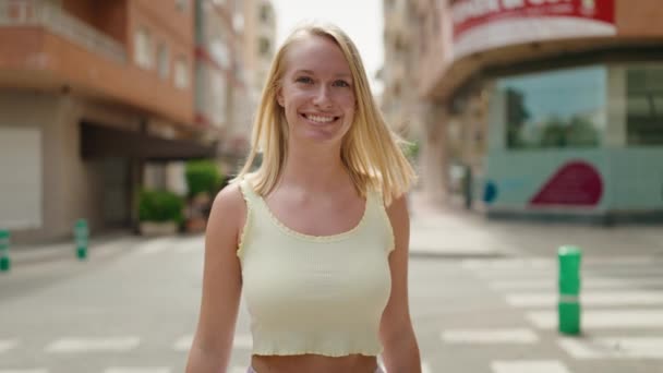 年轻的金发女子带着自信的笑容在街上走着 — 图库视频影像