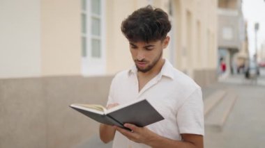 Young arab man smiling confident reading book at street
