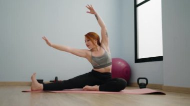 Genç kızıl saçlı kadın spor merkezinde yoga eğitimi alıyor.