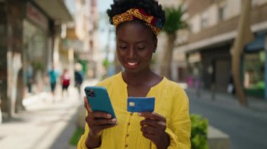 Genç Afrikalı Amerikalı kadın akıllı telefon ve kredi kartı kullanıyor.