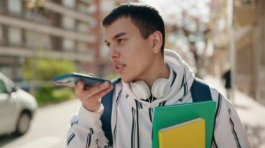 Young man student talking on the smartphone holding books at street