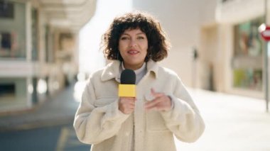 Young hispanic woman news reporter speaking using microphone at street