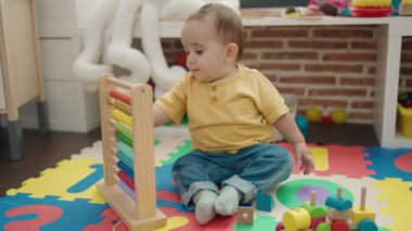 Adorable hispanic baby playing with abacus sitting on floor at kindergarten
