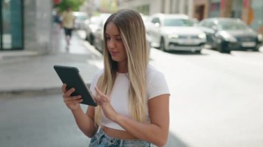 Young beautiful hispanic woman using touchpad with winner expression at street